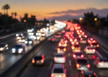 Close-up of blurred freeway headlights and taillights at dawn with traffic backed up in the distance.