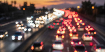 Close-up of blurred freeway headlights and taillights at dawn with traffic backed up in the distance.