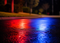 Close-up of blurred police lights reflecting across dark pavement outside a residential area at night.