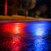 Close-up of blurred police lights reflecting across dark pavement outside a residential area at night.