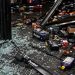 Close-up of broken storefront glass, scattered auto parts and damaged shelving on a dark floor.