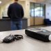 Close-up of car keys beside a sobriety testing device on a CHP office counter, with a blurred person standing in the lobby background.
