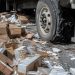 Close-up of cardboard boxes and broken cargo scattered across freeway pavement beside a damaged truck tire.
