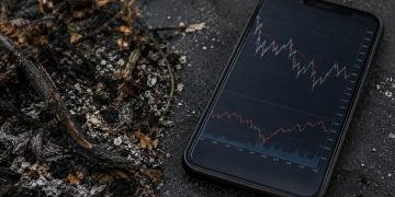 Close-up of charred vegetation and ash beside a smartphone displaying generic market-style lines.