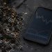 Close-up of charred vegetation and ash beside a smartphone displaying generic market-style lines.