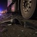 Close-up of damaged vehicle debris beside a big rig tire on freeway pavement at night.