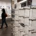Close-up of empty designer eyeglass display stands inside an optical store, with a blurred shopper walking past in the background.