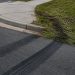 Close-up of fresh tire marks curving toward a sidewalk curb beside flattened grass.