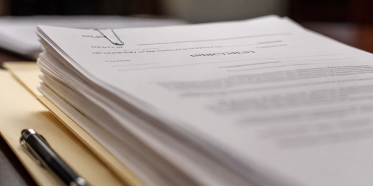 Close-up of legal documents labeled “indictment” resting on a manila folder beside a pen.