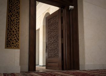 Close-up of mosque prayer rugs and a security camera near an entrance with no identifiable signage.