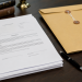 Close-up of official legal paperwork beside a pen and sealed manila folder on a desk.