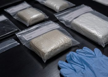 Close-up of sealed evidence packages beside disposable gloves on a dark inspection table.
