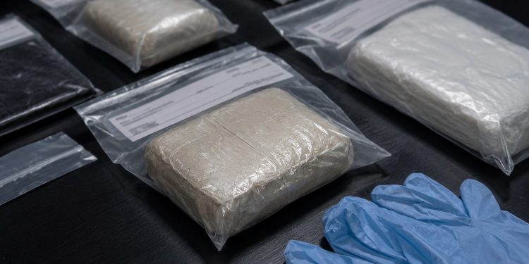 Close-up of sealed evidence packages beside disposable gloves on a dark inspection table.