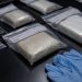 Close-up of sealed evidence packages beside disposable gloves on a dark inspection table.