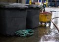 Close-up of sealed waste containers, protective gloves and cleanup equipment on a wet industrial floor.