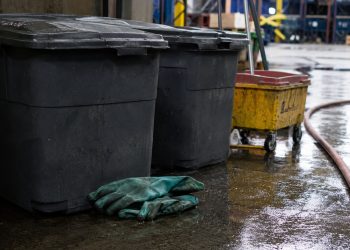 Close-up of sealed waste containers, protective gloves and cleanup equipment on a wet industrial floor.