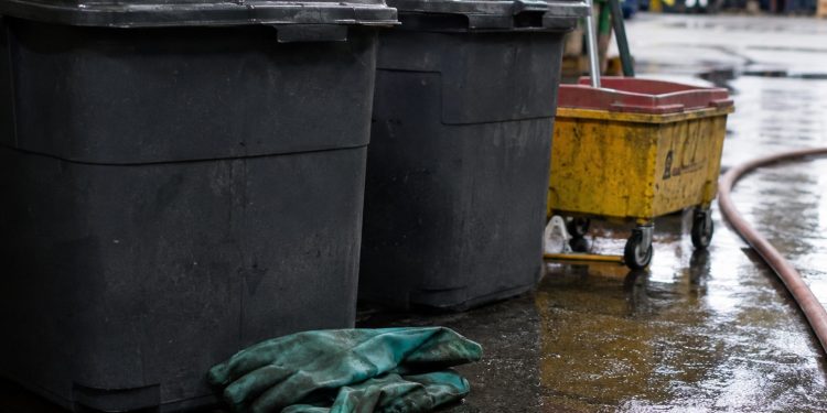 Close-up of sealed waste containers, protective gloves and cleanup equipment on a wet industrial floor.