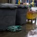 Close-up of sealed waste containers, protective gloves and cleanup equipment on a wet industrial floor.