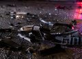 Close-up of shattered vehicle debris and broken plastic pieces scattered across dark pavement at night.