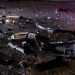 Close-up of shattered vehicle debris and broken plastic pieces scattered across dark pavement at night.