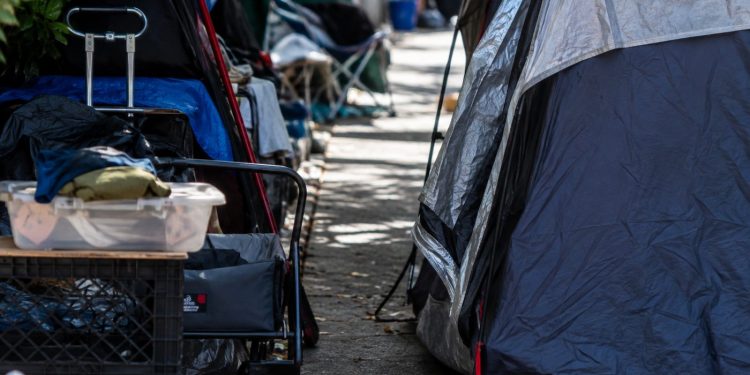 Close-up of tents and personal belongings narrowing a residential sidewalk, with no identifiable homes or street signs.