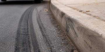 Close-up of tire marks beside a curb with a blurred vehicle and sidewalk in the background.