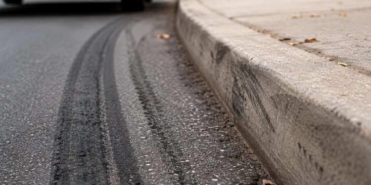 Close-up of tire marks beside a curb with a blurred vehicle and sidewalk in the background.