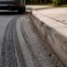 Close-up of tire marks beside a curb with a blurred vehicle and sidewalk in the background.