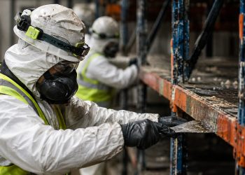 Close-up of workers in protective gear clearing food debris from damaged warehouse shelving.