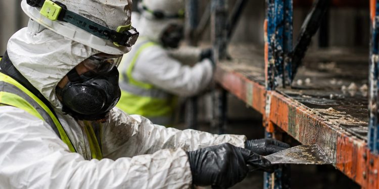 Close-up of workers in protective gear clearing food debris from damaged warehouse shelving.