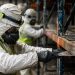 Close-up of workers in protective gear clearing food debris from damaged warehouse shelving.