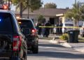 Blurred police vehicles and officers outside a San Bernardino home during an officer-involved shooting investigation, with the residential street in the background.