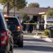 Blurred police vehicles and officers outside a San Bernardino home during an officer-involved shooting investigation, with the residential street in the background.