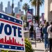 Close-up of a Los Angeles mayoral campaign sign with blurred voters and a city street in the background, illustrating the 2026 mayoral race.
