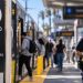 Close-up of a Metro E Line platform with blurred passengers and a uniformed police officer in the background, illustrating expanded transit patrols in Santa Monica.