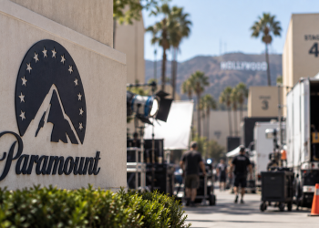 Close-up of a Paramount-style studio lot with blurred Hollywood production activity in the background.