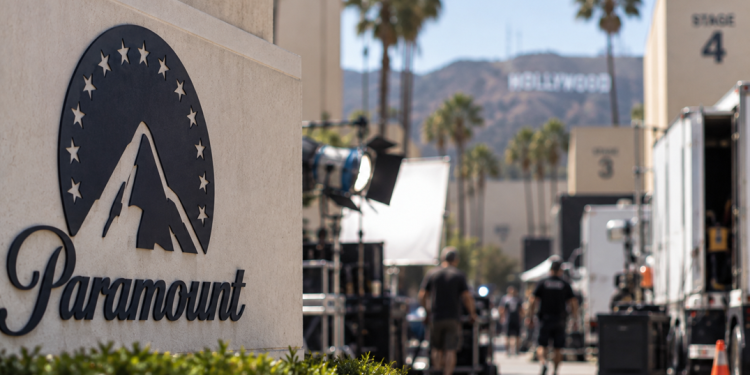 Close-up of a Paramount-style studio lot with blurred Hollywood production activity in the background.