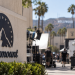 Close-up of a Paramount-style studio lot with blurred Hollywood production activity in the background.