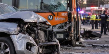 Close-up of a damaged SUV and Metro bus at a Southern California crash scene, with emergency vehicles and investigators blurred in the background.