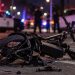 Close-up of a damaged electric bicycle on a Los Angeles roadway at night, with blurred emergency lights and police activity in the background, illustrating a fatal e-bike crash in Arleta.