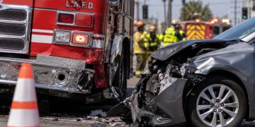 Close-up of a damaged firetruck and civilian vehicle at a South Los Angeles intersection, with traffic cones and blurred emergency responders in the background.