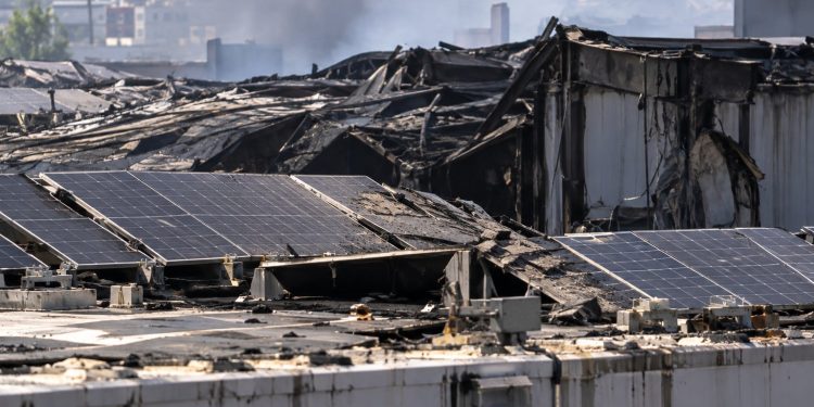 Close-up of a damaged industrial warehouse roof with solar panels and smoke haze in the background, illustrating litigation over the Boyle Heights warehouse fire.