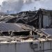 Close-up of a damaged industrial warehouse roof with solar panels and smoke haze in the background, illustrating litigation over the Boyle Heights warehouse fire.