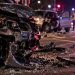 Close-up of a damaged vehicle and roadway debris at night, with blurred emergency lights in the background, illustrating a fatal two-vehicle crash investigation in Encino.