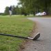 Close-up of a golf club lying beside a cart path, with a blurred golfer and distant police presence visible in the background.