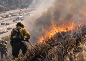 Close-up of a hillside brush fire burning near a freeway, with heavy smoke and firefighters working in the background, illustrating the Getty Fire response in Los Angeles.