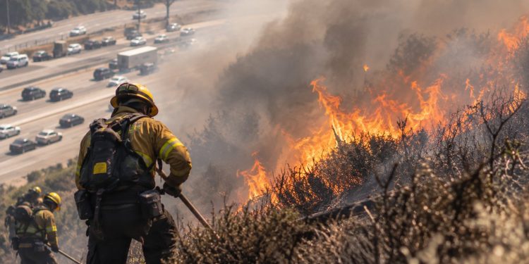 Close-up of a hillside brush fire burning near a freeway, with heavy smoke and firefighters working in the background, illustrating the Getty Fire response in Los Angeles.