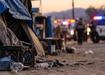 Close-up of a makeshift encampment area with a blurred emergency response in the background, illustrating a stabbing investigation in Hesperia.