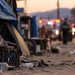 Close-up of a makeshift encampment area with a blurred emergency response in the background, illustrating a stabbing investigation in Hesperia.