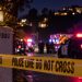 Close-up of a residential street at night with blurred police lights, crime-scene tape and emergency responders in the background, illustrating an officer-involved shooting in the Hollywood Hills.